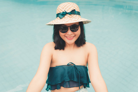 美丽的女人在游泳池娱乐户外和暑假放松的肖像。 漂亮的女人穿着泳衣，戴着帽子，在池边放松日光浴。 暑假概念。