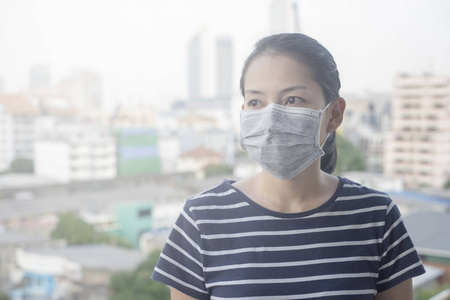因城市空气污染而戴N95口罩的妇女，有微粒物质或PM2.5，有城市建筑背景