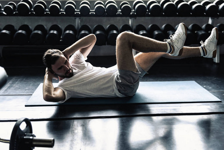 运动男在健身馆锻炼的肖像，运动男在哑铃前做仰卧起坐或骑自行车锻炼的肖像，健康和保健概念。