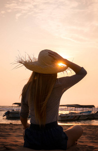 戴着帽子的年轻女子看着大海中的夕阳