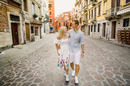 年轻漂亮的情侣女孩穿着礼服，穿着白色衬衫的男人走过意大利威尼斯的街道