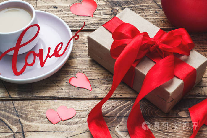 s day. gift box with red bow and cup of coffee on wooden table.