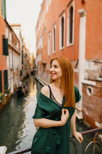 意大利美丽的威尼斯城市的阳台上站着一个年轻漂亮的女孩，她的头发是红色的，裙子是绿色的