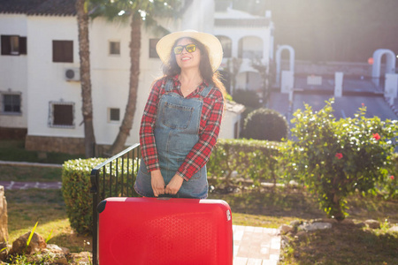 旅行旅游和人的概念戴帽子的快乐年轻女子拿着一个巨大的红色行李箱, 微笑着越过自然背景