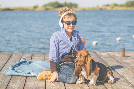小可爱的男孩和他的狗坐在河边。 他们在一个美丽的晴天一起享受。 男孩和他的小狗玩。 长大后喜欢动物，狗，空闲时间旅行度假。 复制