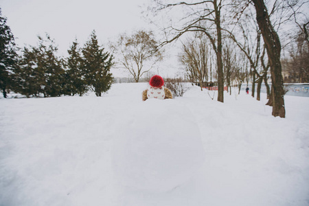 冬天的小女孩穿着温暖的衣服和帽子，遮住脸躲在雪球后面，在雪地公园或森林里。 假日的冬季乐趣休闲。 家庭生活方式观念