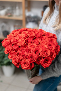 红玫瑰在玻璃花瓶在妇女的手中。鲜红红的花店里花店的概念。壁纸
