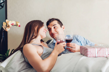 一对相爱的夫妇早上躺在床上喝酒。 快乐的人们庆祝情人节