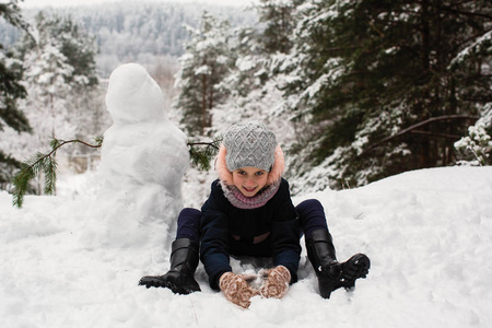 可爱的小女孩在冬天下雪的公园里堆雪人。