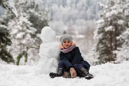 可爱的小女孩在冬天下雪的公园里堆雪人。