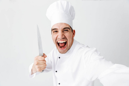 快乐厨师穿着制服站在白色背景上自拍，拿着刀