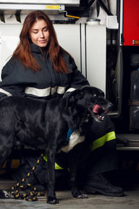 坐在消防车背景上的女消防队员与黑狗的肖像
