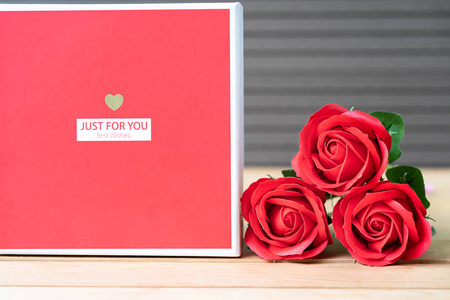 将红色玫瑰和心形盒子贴在木头背景上，情人节的概念是玫瑰和红色心形盒子