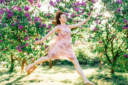美丽的少女穿着粉红色的裙子在夏日盛开的公园里跳跃