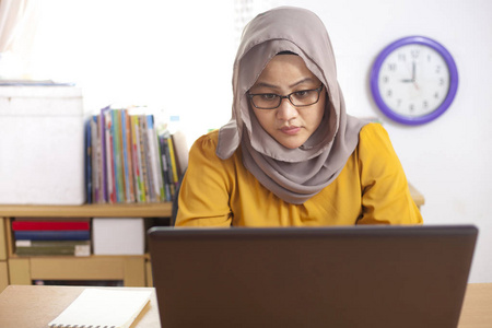 亚洲穆斯林女商人在办公室笔记本电脑上工作的肖像，微笑着，快乐的表情