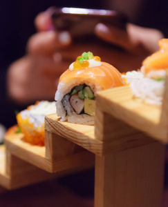 女性使用智能手机拍摄日本新鲜鱼食物鲑鱼寿司卷装饰在传统日本餐厅的木制台阶上。 丰富鱼类营养理念的健康食品