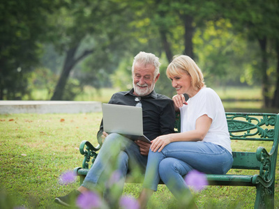 两个快乐的老年人退休，男人和女人坐在公园里使用电脑笔记本电脑