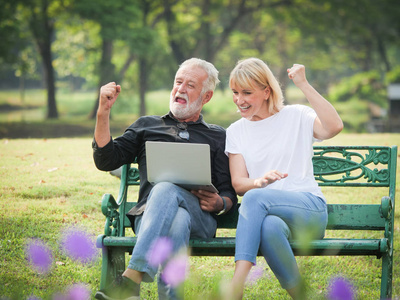 两个快乐的老年人退休了男人和女人坐在公园里使用电脑笔记本电脑