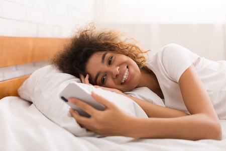 快乐的女孩在床上的智能手机发短信