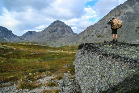 年轻的男性游客用苔藓覆盖的石头拍摄一座美丽的山。