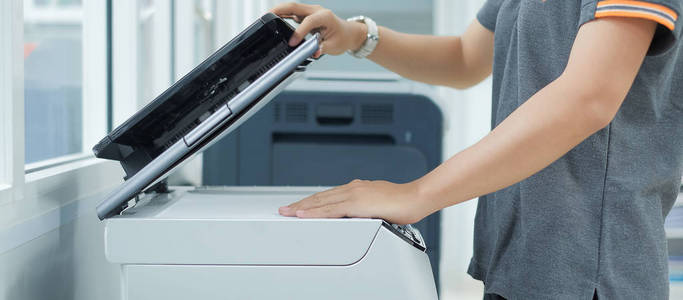 商务女性在办公室用手将文件纸放入打印机扫描仪或激光复印机