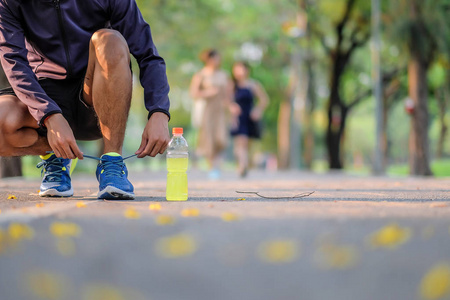 年轻运动员男子在公园室外系跑鞋，男跑运动员准备在外面的路上慢跑，亚洲健身步行和早上在人行道上锻炼。健康和体育概念