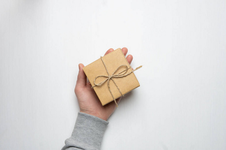 s hand holds a gift in a box on a white wooden background