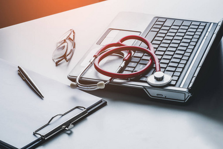 笔记本电脑上的听诊器和眼镜，带有剪贴板空白纸医生在线医学概念