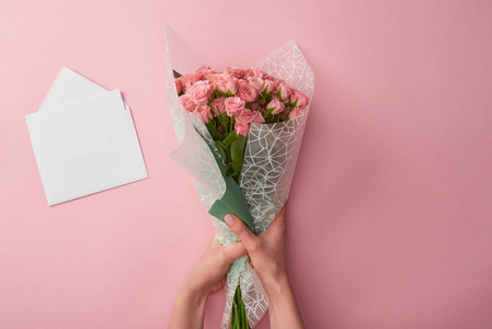 一个女人拿着一束美丽的玫瑰花和一个白色信封，被隔离在粉红色上