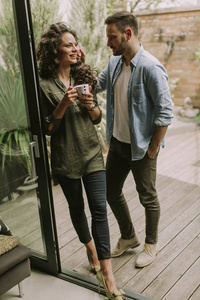 幸福的年轻可爱的一对相爱的夫妇拥抱在一起，在家门口的窗户边喝咖啡