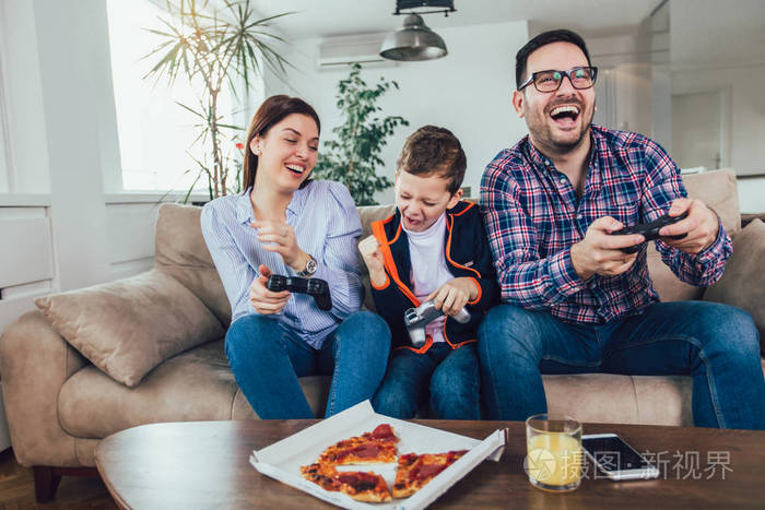 幸福的一家人坐在沙发上玩电子游戏,吃披萨