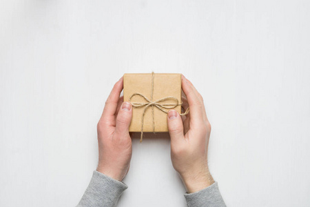 s hands holds a gift in a box on a white wooden background