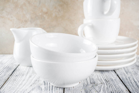 分类堆叠干净，空的，新的白色厨房用具，盘子，碗，杯子。 在白色混凝土背景上