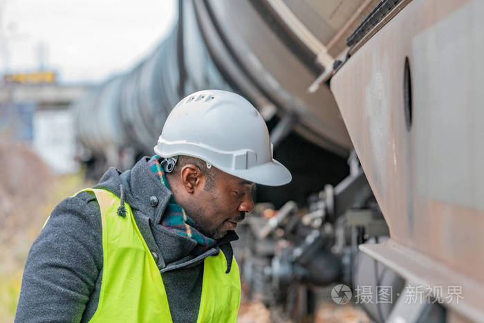 非洲裔美国铁路工程师戴着安全装备(头盔和夹克)检查齿轮列车