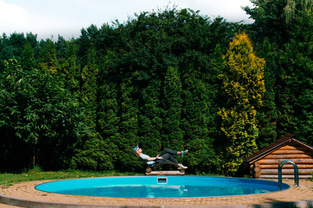 在西西里岛别墅的游泳池外的躺椅上放松的男人，背景是绿色的南方树墙