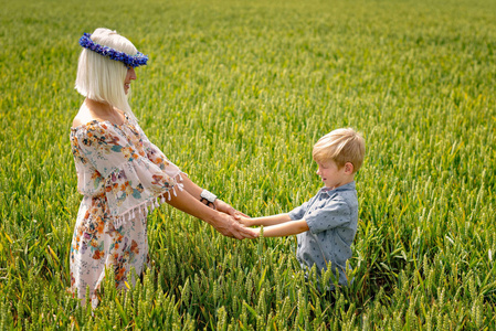 一个金发女人，一个儿子牵着手，在谷物领域。