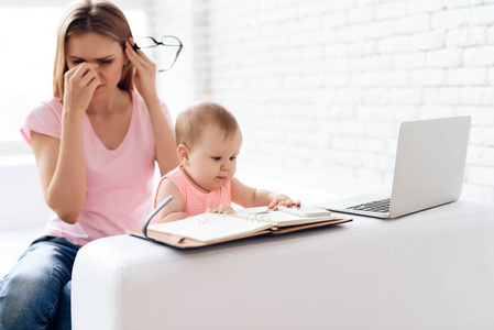 疲惫的母亲带着婴儿工作和使用笔记本电脑