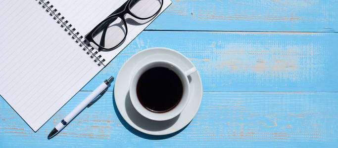  pen, notebook and eyes glasses on blue wooden table background.