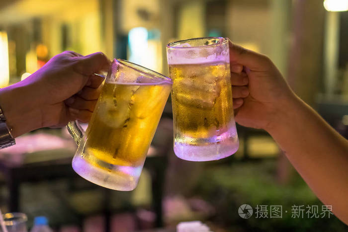 两杯啤酒在低灯光酒吧和餐馆的朋友之间一起干杯. 放松和喝酒的概念