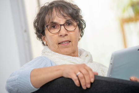 一位迷人的深黑色头发的女士，戴着眼镜，在家里用数码平板电脑
