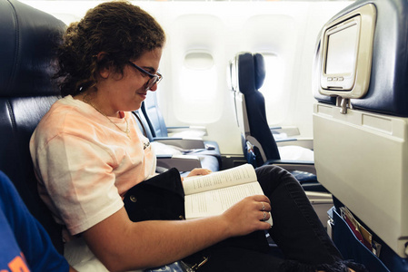 年轻女子微笑, 而阅读飞机内的书