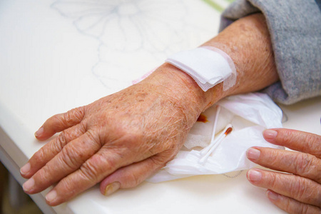 将老妇人的手上肢或手臂靠近伤员，等待护士治疗伤口，包扎病人的鲜血和盐水。