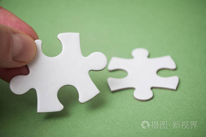 男人用手连接两个拼图块在绿色背景上.