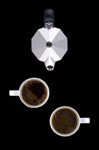 咖啡壶和两个白色杯子在一个黑色背景的碟子上。