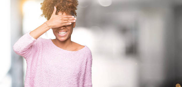 美丽的年轻非洲裔美国妇女戴着眼镜，在孤立的背景上微笑，用手笑，遮住眼睛，以获得惊喜。 盲目的概念。