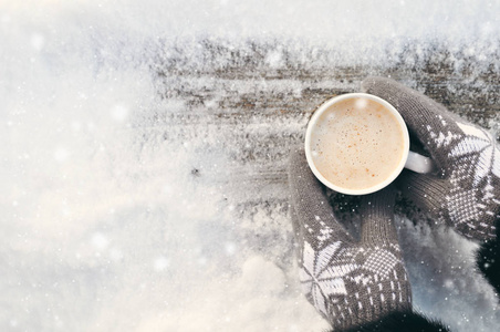 冬天的图片双手穿着针织灰色手套，在下雪的一天，在村里的一个木制乡村背景上拿着一杯热咖啡。 共空间。
