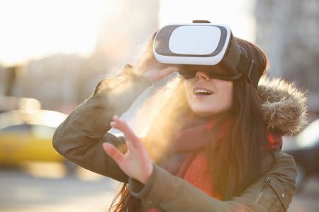年轻女性在日落时分在户外为移动游戏应用程序玩超级酷的虚拟现实眼镜。使用带有创新VR耳机的移动应用程序