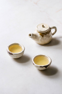 热绿茶在两个传统的中国粘土陶瓷杯和茶壶站在白色大理石桌子上。