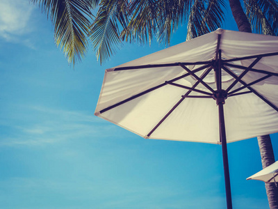 带椰子棕榈树的白色雨伞，带海洋，蓝天背景，供旅行和度假使用