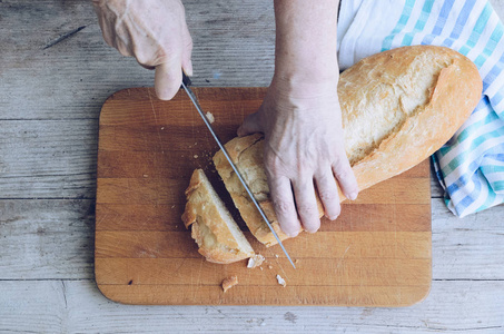 高级妇女在农村厨房桌子上的木板上切新鲜烘焙的面包。 传统的面包店概念。 乡村复古风格。 上面的风景。